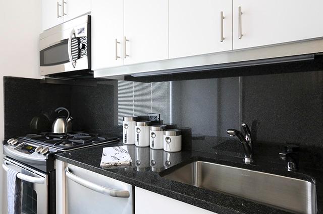 An updated kitchen with black countertops and backsplash with white cabinetry in a New York City apartment.